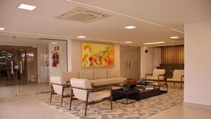 Un hall d’entrée moderne avec un canapé, des fauteuils, une table basse et un tableau abstrait aux couleurs vives.