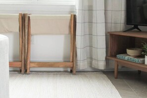 A room with a wooden stand, a white rug, a shelf with a bowl and a plant, and a television on a stand.