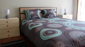 Un letto rifatto con cura, una coperta a motivi decorativi, due comodini con lampade e una cassettiera.