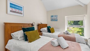 A bedroom with two beds, each with a wooden headboard, white bedding, and colorful pillows. There is a window with a view of greenery outside. - Apartment 4 St Mary's House - Short Walk to Beach (Tenby)