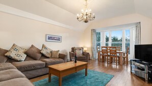 A spacious living room with a wooden coffee table, a sofa set, a dining area with chairs and a table, a television, and a chandelier. - Apartment 4 St Mary's House - Short Walk to Beach (Tenby)