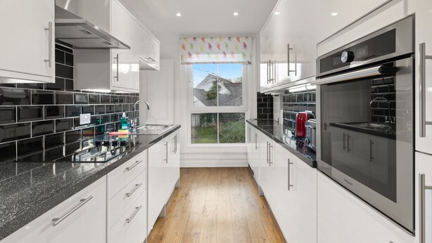 A modern kitchen with white cabinets, black countertops, and stainless steel appliances. - Apartment 4 St Mary's House - Short Walk to Beach (Tenby)