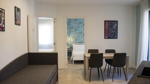 Un espacio habitable moderno y compacto con sofá, mesa de comedor con sillas, cama y pequeña kitchenette.