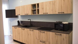 Una cocina moderna con armarios de madera, encimera negra, microondas integrado y televisor de pantalla plana montado sobre los armarios.