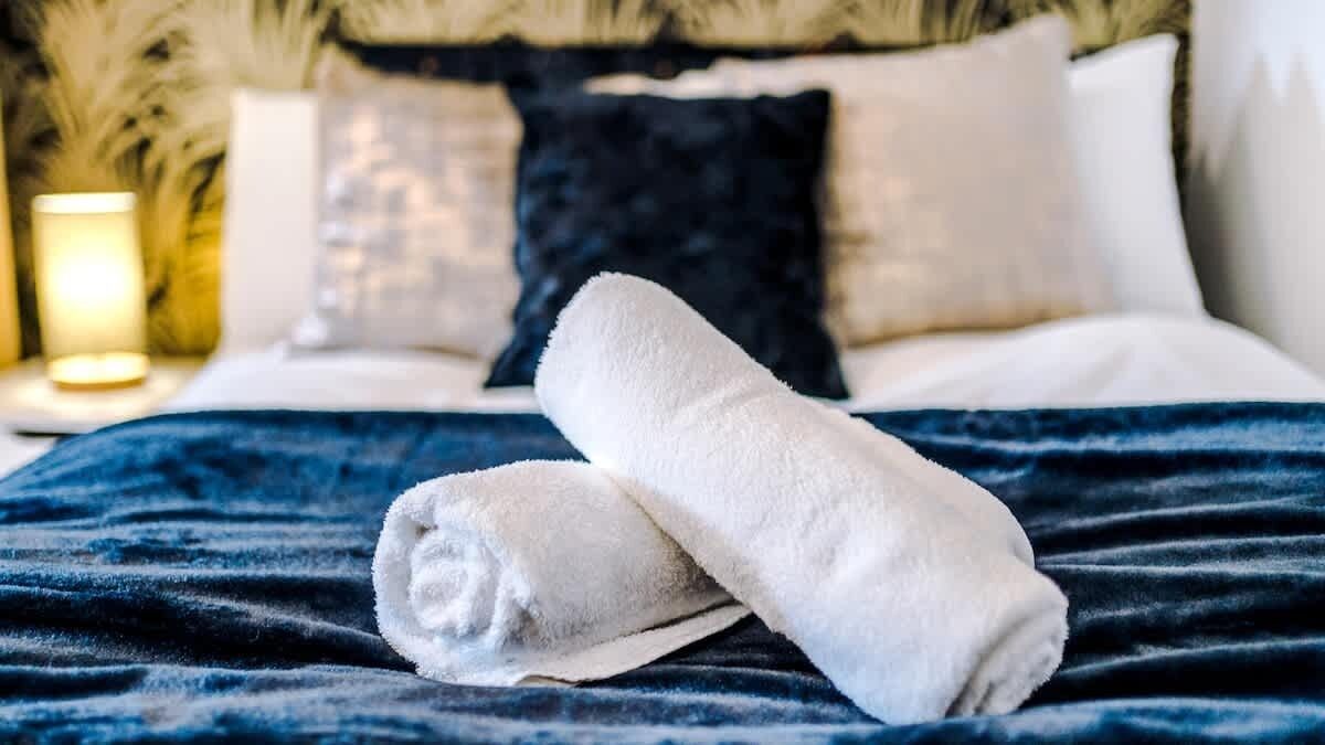 Una cama bien hecha con una manta azul y dos toallas blancas.