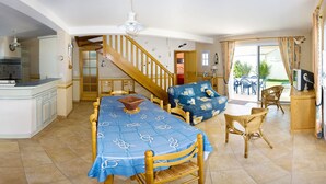 A spacious kitchen with a central island, a dining area with a blue tablecloth, and a staircase leading to an upper level. - Maison 60 Mètres mer et Plage (Saint-Denis-d'Oléron)