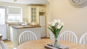 A dining area with a wooden table, white chairs, a vase with white flowers, and a wall clock. - 3 bedroom accommodation in Easington, near Staithes (Easington, near Staithes)