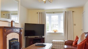 A living room with a fireplace, a television, a sofa, and a window with curtains. - 3 bedroom accommodation in Easington, near Staithes (Easington, near Staithes)