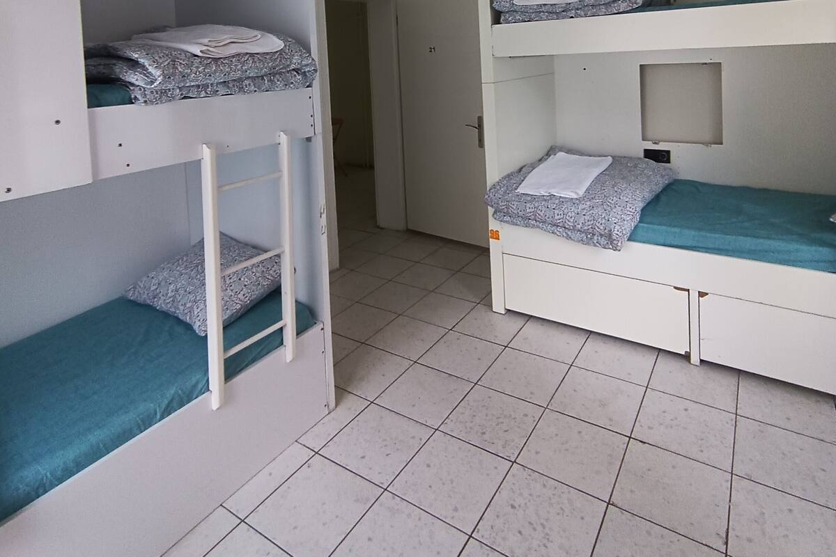 Un dormitorio con literas, ventilador de techo y una puerta que da a otra habitación.