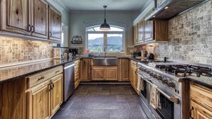 A kitchen with wooden cabinets, a large window, and a view of mountains. - Luxury Family Cabin | Hot Tub, Game Room & Views (Gatlinburg)