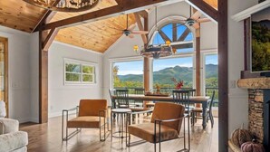 A spacious room with a high ceiling, wooden beams, a fireplace, and a large window offering a mountain view. - Luxury Family Cabin | Hot Tub, Game Room & Views (Gatlinburg)