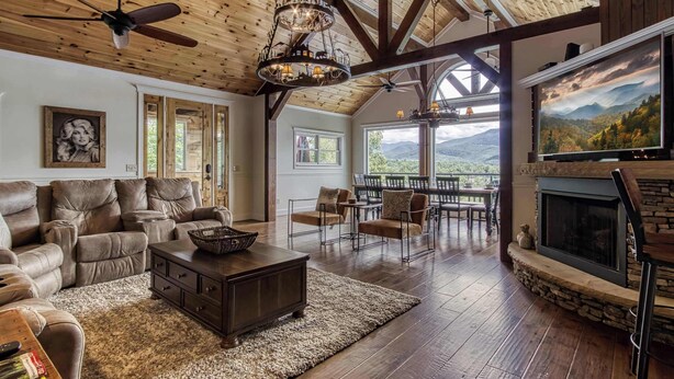 A spacious living room with a fireplace, leather sofas, and a large TV screen. - Luxury Family Cabin | Hot Tub, Game Room & Views (Gatlinburg)