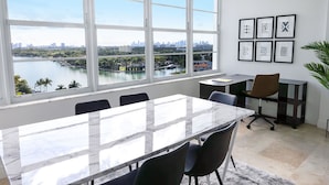 A conference room with a large window offering a view of a city skyline and water. There are framed abstract artworks on the wall. - 2bd Beachfront Master Ste, Bay View w/balcony, Pool, nearby dining, beach access (Miami Beach)