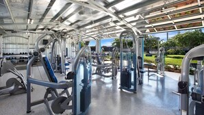 A covered gym with various exercise machines, a clear view of the outdoors, and a spacious layout. - Steps from Beach, Stunning View, A/C, Pool Access (Koloa)
