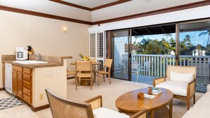 A modern kitchen with a sink and a coffee maker, a dining area with wicker chairs and a round table, and a balcony with a view of palm trees. - Steps from Beach, Stunning View, A/C, Pool Access (Koloa)