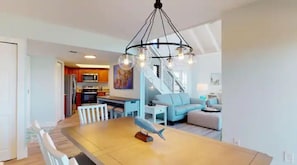A modern kitchen with a dining area, a staircase, and a living room with a blue sofa.