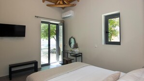 A bedroom with a bed, a TV mounted on the wall, a window, and a door leading to an outdoor area. - Irini Villa by Elrin Villas Mani (West Mani)