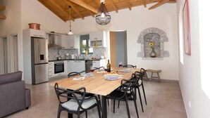 A modern kitchen with a wooden ceiling, a dining area with a wooden table and chairs, and a stone fireplace. - Irini Villa by Elrin Villas Mani (West Mani)