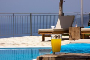 Blick auf ein Schwimmbecken mit Orangensaft, Liegestühlen und einer Holzterrasse.
