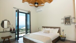 A bedroom with a wooden ceiling, a large bed, a nightstand, a mirror, and a view through a glass door. - Irini Villa by Elrin Villas Mani (West Mani)