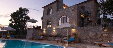 A stone building with a swimming pool, outdoor seating, and a staircase leading to a balcony.
