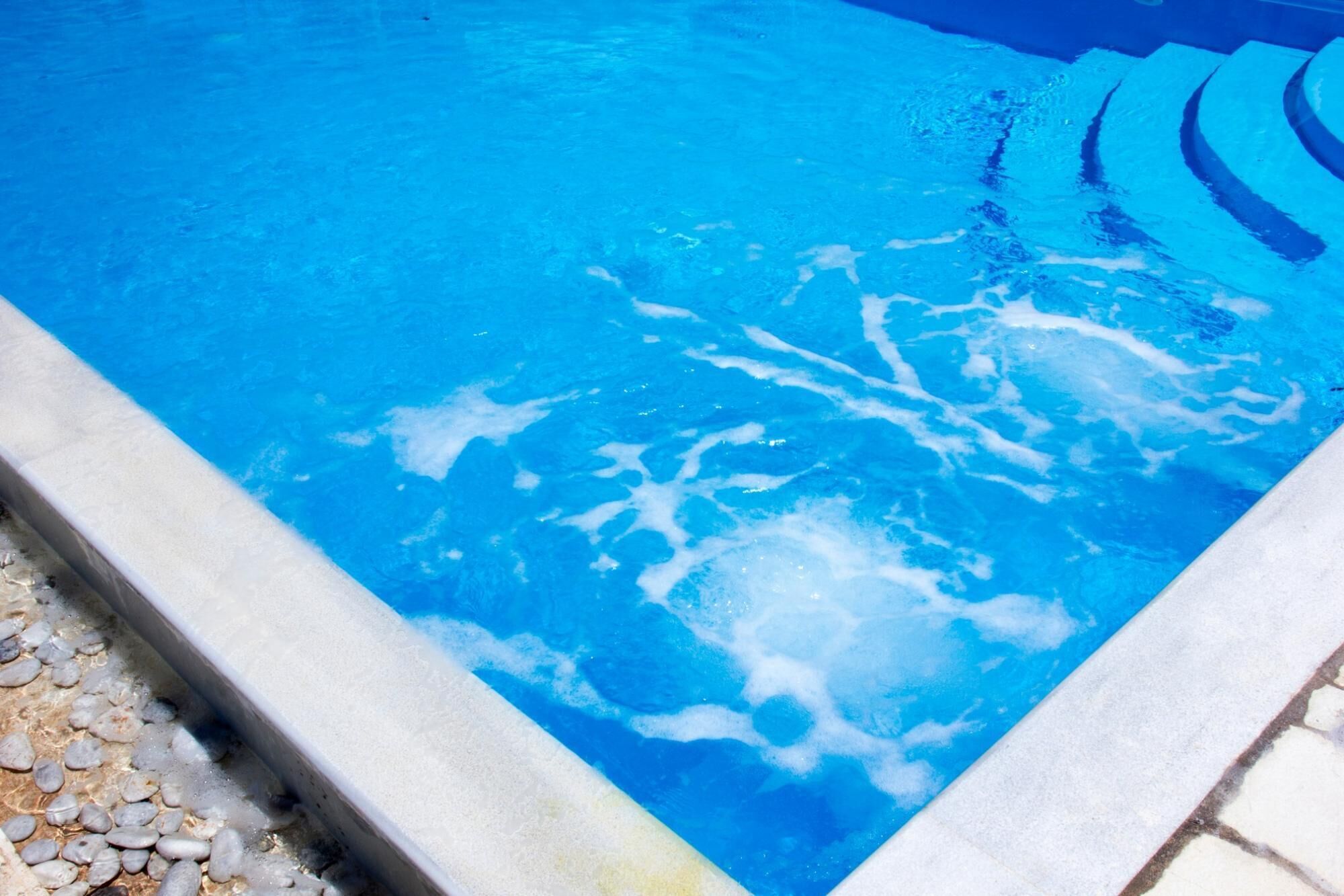 A swimming pool with clear blue water and visible foam patterns.