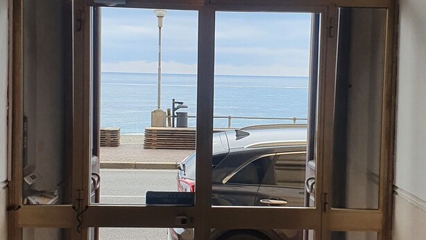 Vista attraverso una porta di vetro sull'oceano e un'auto parcheggiata all'esterno.