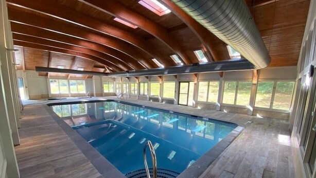 A large indoor swimming pool with a wooden ceiling and large windows.
