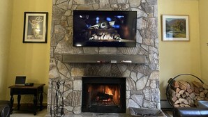 A stone fireplace with a TV mounted above it, a framed picture on the wall, and a laptop on a small table.