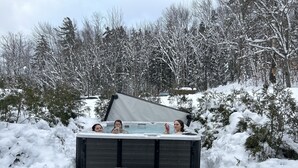 A hot tub in a snowy outdoor setting surrounded by snow-covered trees.