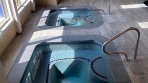 Two hot tubs with built-in seating, surrounded by a covered patio area with large windows.