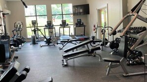 A gym with various exercise equipment, large windows, and a television screen.