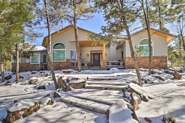 A house with a stone foundation and a wooden roof, surrounded by snow-covered ground and trees. - Patio & Forest View: Peaceful Show Low Home (Show Low)