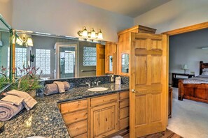 A bathroom with a granite countertop, wooden cabinets, a large mirror, and a shower area. - Patio & Forest View: Peaceful Show Low Home (Show Low)