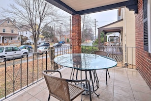 Relax in an outdoor seating area with a round table and two comfortable chairs, surrounded by a brick pillar and a metal railing.