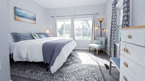 Une chambre à coucher avec un lit, une chaise, une commode et une fenêtre avec des rideaux.