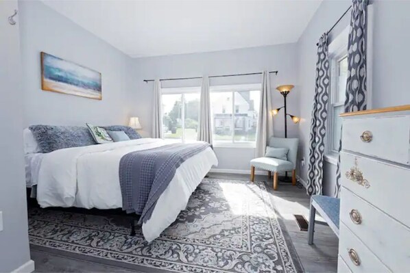 A bedroom with a bed, a chair, a dresser, and a window with curtains.