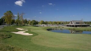 Un parcours de golf avec des bunkers, un étang et un bâtiment en arrière-plan.
