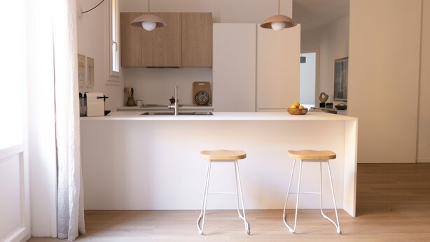 Een moderne keuken met een centraal eiland, twee barkrukken, hanglampen en houten kastjes.