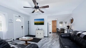 A modern living room with a black leather sofa, a ceiling fan, a white cabinet, and a dining area in the background. - THE PEACEABLE NEST - Buffalo/Niagara Akron, NY (Newstead)