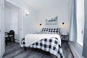 A bedroom with a checkered bedspread, two bedside lamps, a small table, and a chair.
