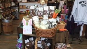 A display of various packaged goods, including snacks and beverages, arranged on a wooden stand in a store. - THE PEACEABLE NEST - Buffalo/Niagara Akron, NY (Newstead)