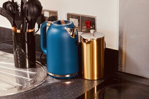 A kitchen counter with a blue kettle, a gold pot, and a utensil holder.