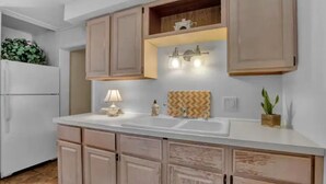 Una cocina con armarios de madera clara, encimera blanca, pileta doble y un estante con adornos.