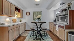Una cocina con armarios de madera, una isla central con taburetes, un horno empotrado y un reloj en la pared.