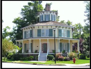 Une maison à deux étages dotée d’une véranda qui fait le tour de la maison, d’une tourelle et d’une entrée surélevée par quelques marches.