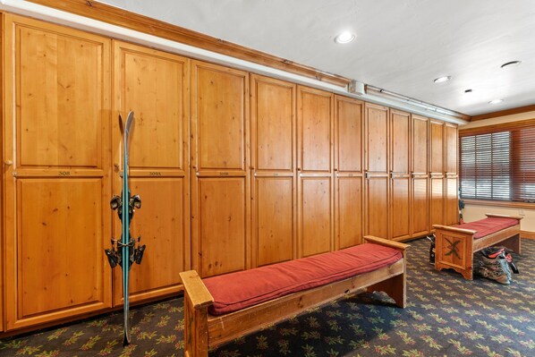 A room with wooden cabinets, a bench, and a pair of skis.