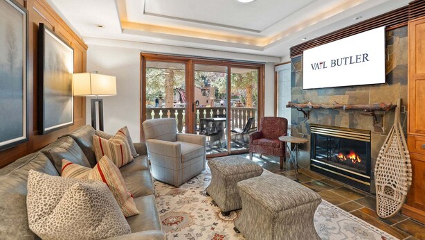 Una sala de estar con chimenea, un sofá, un sillón y una televisión mostrando 'VAIL BUTLER'.