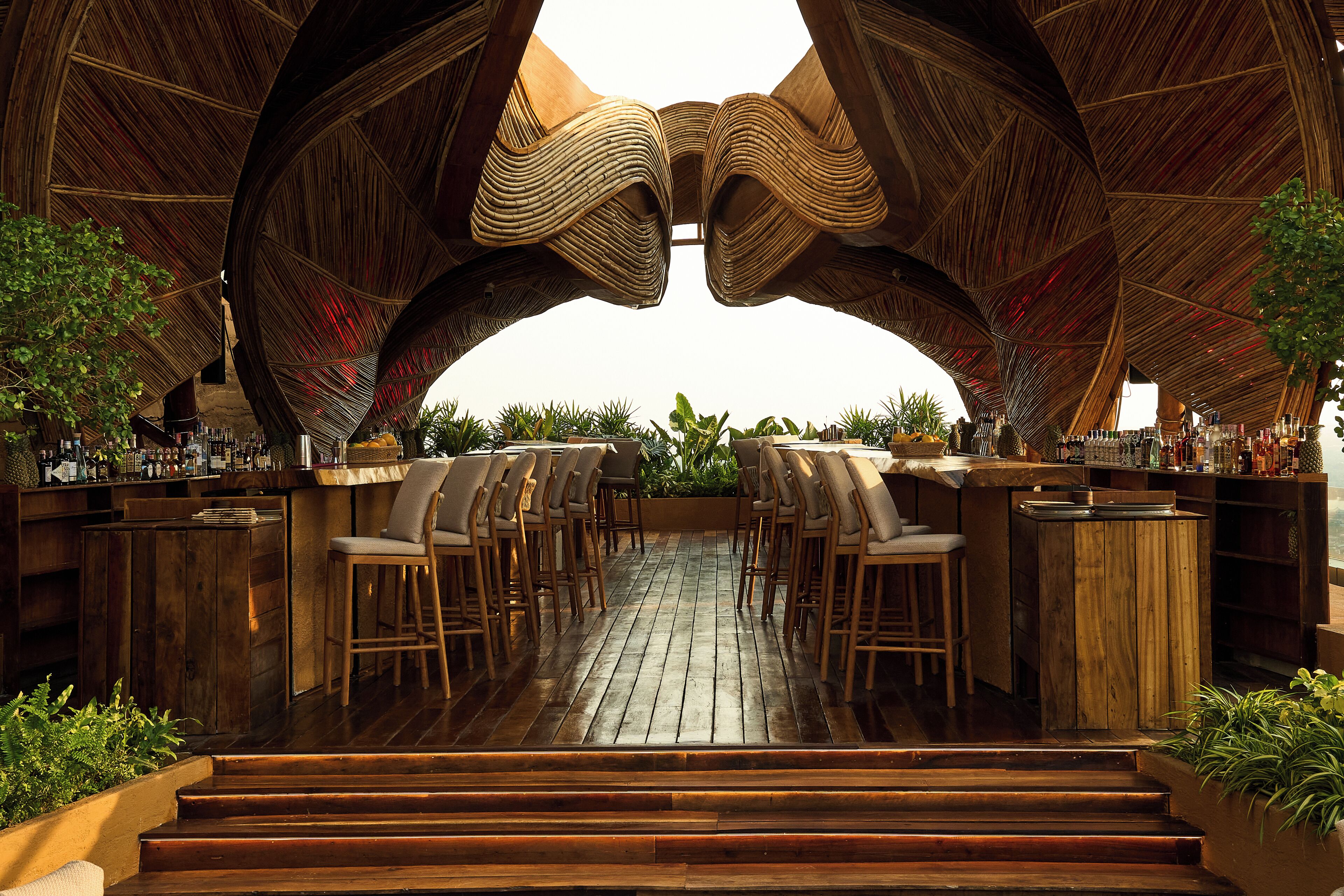 An outdoor bar area with wooden flooring, bar stools, and a unique arched ceiling structure.