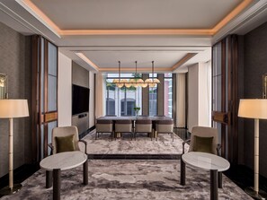 A modern hotel room with a dining area, a flat-screen TV, and a large window with a view of the city.